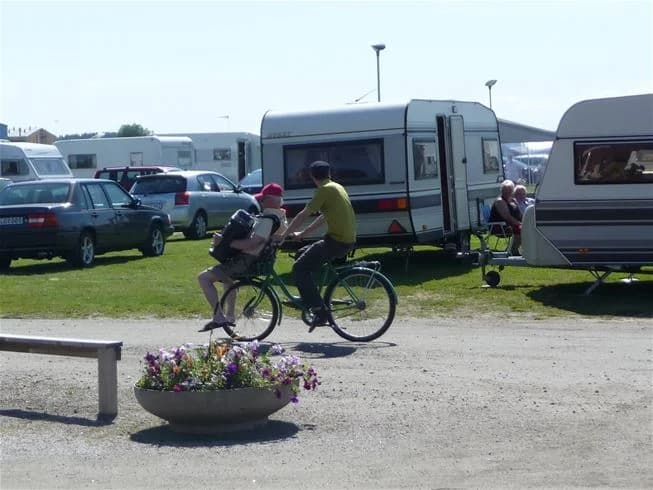 En grupp cyklar står parkerade vid en campingplats. I bakgrunden syns husbilar och tält, vilket ger en känsla av friluftsliv och rekreation vid Västra Kajen Camping.
