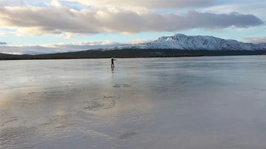 En vinterlandskap som visar ett fridfullt panorama av Vålågårdens Värdshus & Camping, med snötäckta berg i bakgrunden och en frostig sjö som speglar den klara morgonhimlen.