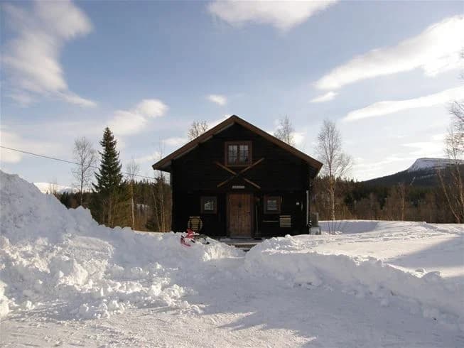 Ett träbeklätt värdshus i ett vinterlandskap med snö på marken. Byggnaden har en synlig ytterdörr och liknar en timmerstuga med sidospårspanel.
