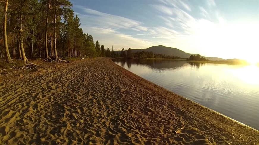 En naturskön vy vid Vålågårdens värdshus & camping visar en spegelblank sjö under en klar himmel, omgiven av grönskande stränder och vacker natur.