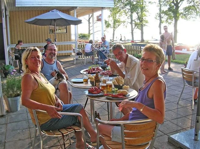 En utomhusmiljö vid Vadstena camping med flera bord och stolar avsedda för avkoppling och sällskap. Solens ljus skapar en inbjudande atmosfär för besökare att sitta och njuta av den natursköna omgivningen.