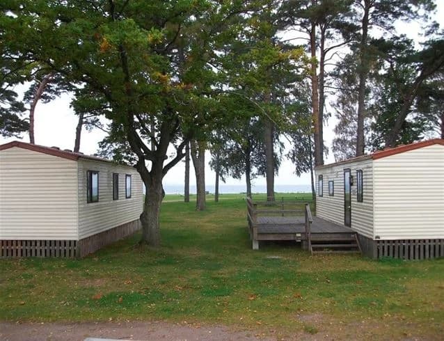 En grön gräsmatta med skuggiga träd på Vadstena camping, perfekt för avkoppling och semesternöje.