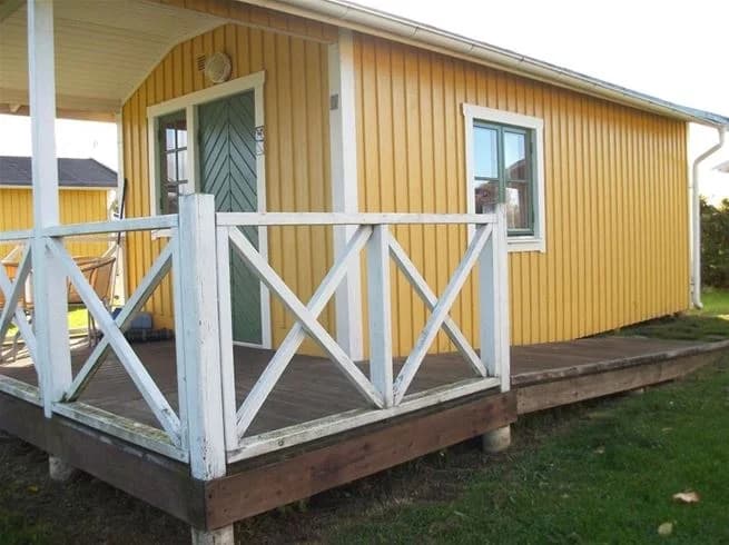 En trästuga vid Vadstena camping med veranda och trappsteg, omgiven av natur.