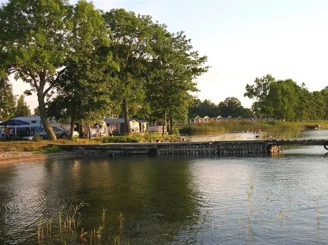 En somrig bild av Vadstena Camping vid en lugn vattenväg, omgiven av träd och grönska.