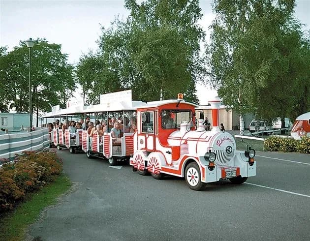 Alt-text: Ett gammalt ånglok står uppställt på Vadstena camping som en del av besöksmålet, omgiven av grönska och en klar himmel.