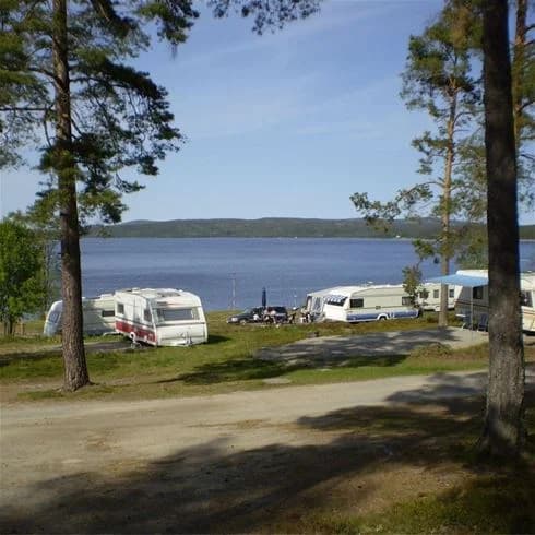 En kustnära camping vid en lugn vik, omgiven av naturlig skönhet med sandstrand och sjöutsikt.
