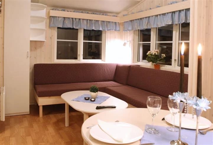 En träbeklädd interiör på Sveg Camping med trägolv. Rummet har ett tak i trä, en soffa, och fönster med gardiner.