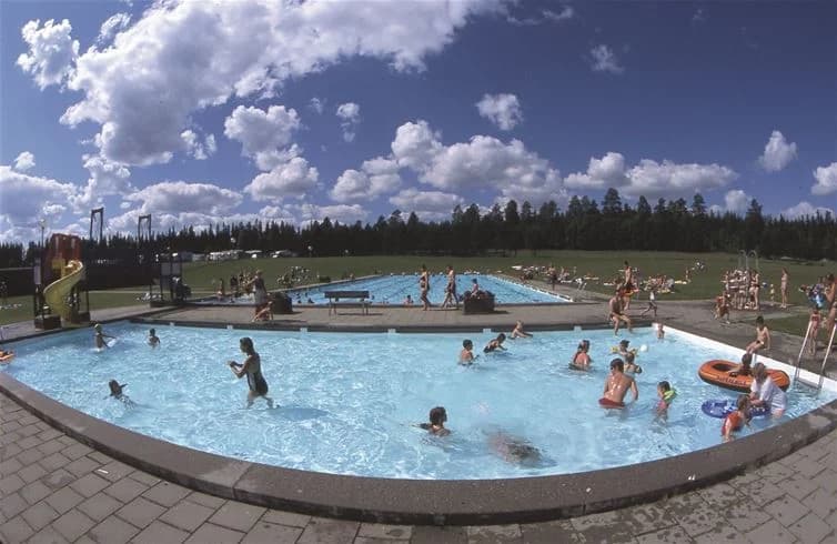 En grupp människor njuter av sin ledighet vid en utomhuspool på Strömsunds camping. Soliga semesterdagar med bad och avkoppling i en parkmiljö.