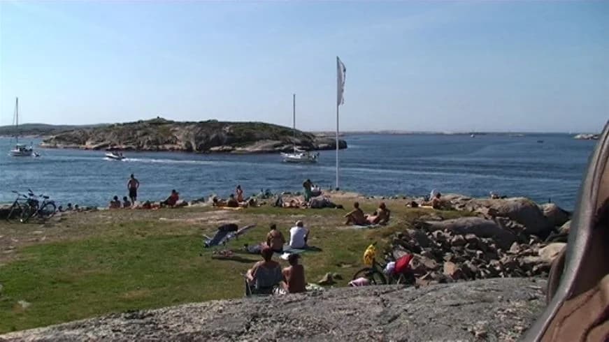 Bild av Sotenäs camping med en kustlinje i bakgrunden, där kusten och havet möts. Stranden omges av en vik och klippiga uddar, vilket skapar en naturskön miljö för semester och rekreation.