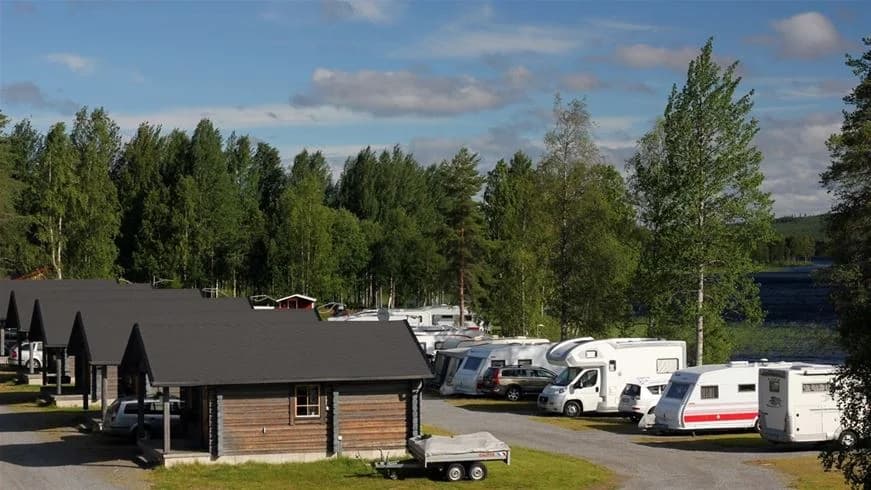 En naturskön campingplats med stugor och husvagnar, omgiven av lummiga träd och en våtmark.