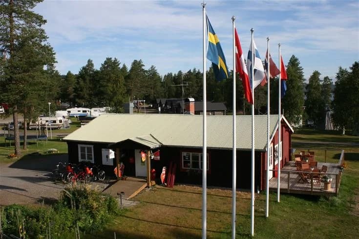 En campingplats med grönskande gräsmatta och flera tält uppställda. Skuggiga områden av träd och stolpar som bär amerikanska flaggor syns i bakgrunden.