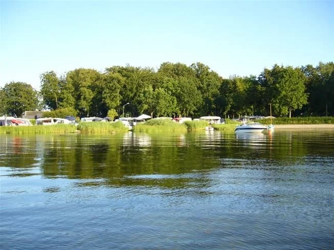 En båt flyter på en lugn vattenväg vid Norje Boke Camping, omgiven av sommarliv och grönska.