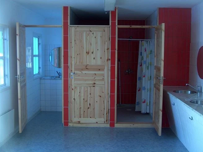 Ett enkelt rum med träinredning på naturcamping Lagom, med trägolv, träväggar och ett trätak. En dörr syns i bakgrunden.