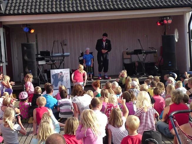 En grupp barn som deltar i en underhållande och lekfull scenföreställning på Möllstorps camping, omgivna av publik i en avslappnad och glädjefylld atmosfär.