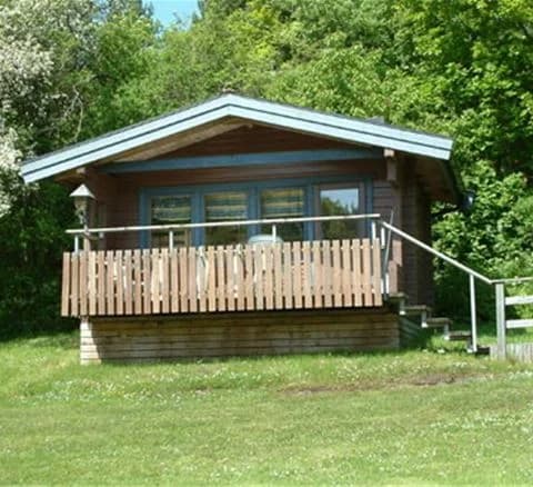 En trästuga med veranda på Marstrands familjecamping, omgiven av grönska och en välskött gård.
