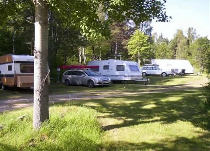 En campingplats med flera husvagnar och bilar parkerade bland träden på Ljusnefors camping.