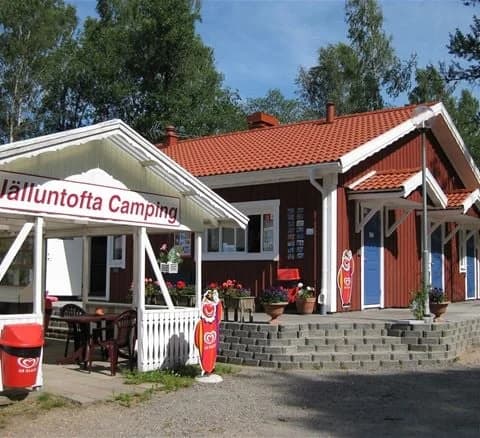 En stuga omgiven av träd och skugga vid Jälluntofta camping, med utemöbler och ett picknickbord på gården, skapar en avkopplande atmosfär för besökare.