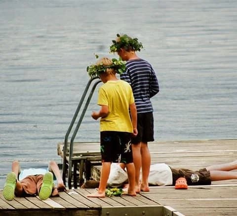 En grupp personer är vid en sjö under sommaren, klädda i shorts, och njuter av fritidsaktiviteter och semester vid Jälluntofta camping.