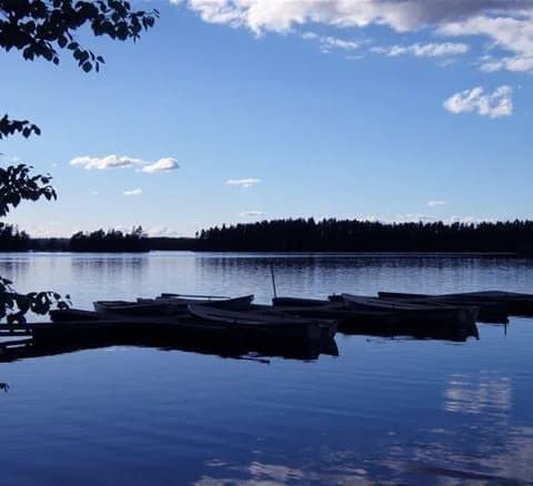 En klarblå himmel speglas i en stilla sjö vid Jälluntofta camping, omgiven av grönskande natur och en vidsträckt horisont.