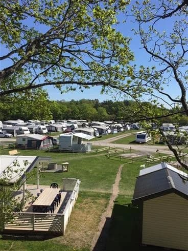 Flygbild över Jogersö Eco Camping visar en pittoresk campingplats med flera husvagnar och bilar parkerade på ett grönskande landskap, omgiven av en blandning av grönska och öppna ytor, vilket ger en inbjudande atmosfär för besökare.