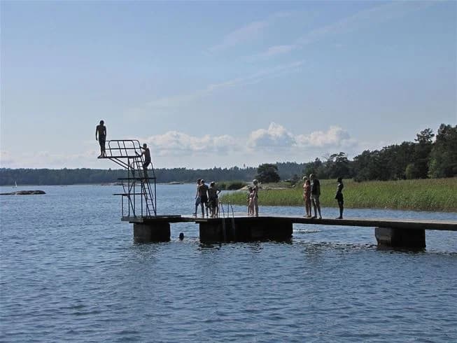 En sjö med en träbrygga som sträcker sig ut över vattnet, omgiven av grönska, på Jogersö Eco Camping. Perfekt för avkoppling och vattenaktiviteter i en naturskön miljö.