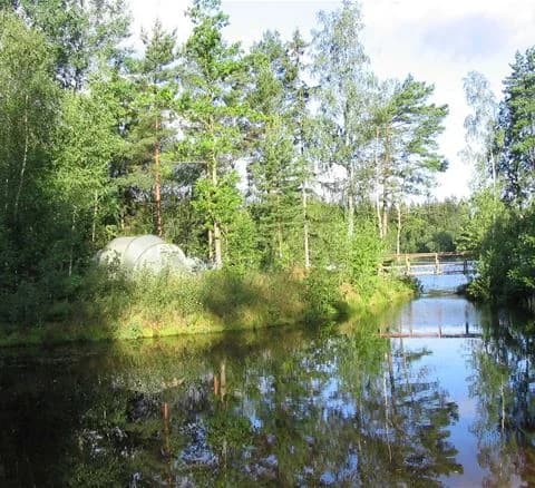 En lugn vattenspegel omgiven av frodig grönska och träd vid Hätteboda vildmarkscamping.