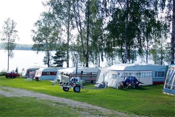 En campingplats med flera uppställda husvagnar och fritidsfordon omgivna av grönska, typisk för Frykenbadens Campings natursköna miljö.