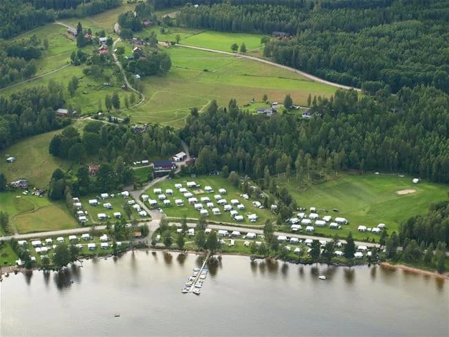 En campingstuga vid Ekeby camping omgiven av träd, med en båt liggande nära en sjö i bakgrunden.