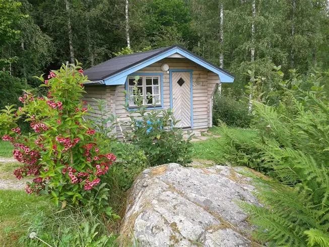 Bild av Ekeby Camping med en stuga och lummig omgivning, inklusive buskar och växter, i en naturskön och lantlig miljö.