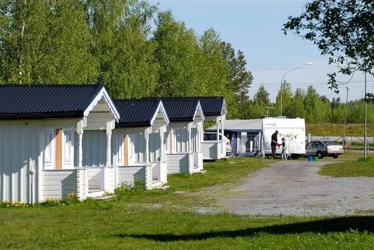 En pittoresk stuga med rött tak och vita väggar omgiven av en grön gräsmatta på Krokomvikens camping under en klar blå himmel.