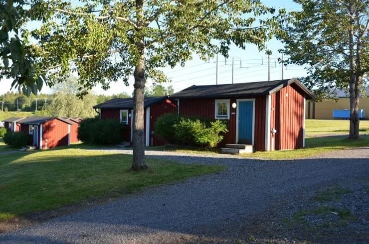 En idyllisk campingplats i Vännäs med grönskande gräsområden och flera små stugor med röda tak, belägen i ett lantligt bostadsområde.