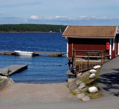 En naturskön vy av Örnäs camping med en vattenväg i förgrunden. På vattnet syns några båtar, och längs kusten finns charmiga stugor omgivna av grönska.