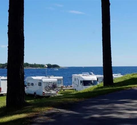 En naturskön vy över vatten vid Örnäs Camping med kustlinje och en strand i förgrunden samt båtar på vattnet.