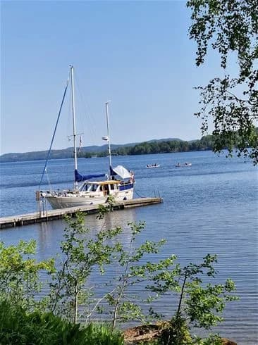 En bild av Laxsjöns camping med flera båtar på det stilla vattnet, omgivna av natursköna kustlandskap och en klar himmel.