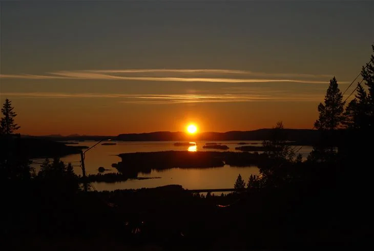 En solnedgång över en stilla sjö vid Storumans camping, med en himmel färgad i orange och rosa nyanser.