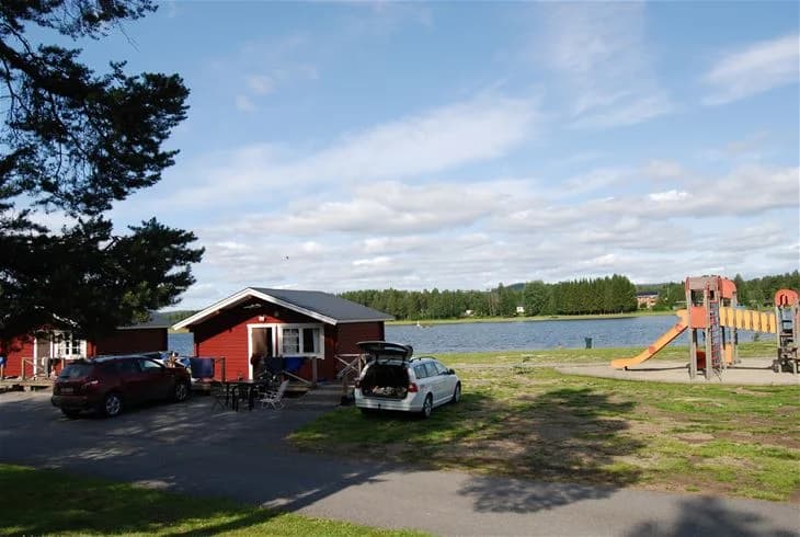 En bild av Storumans camping med en vy över en sjö omgiven av skogsklädda kullar och en molnig himmel.