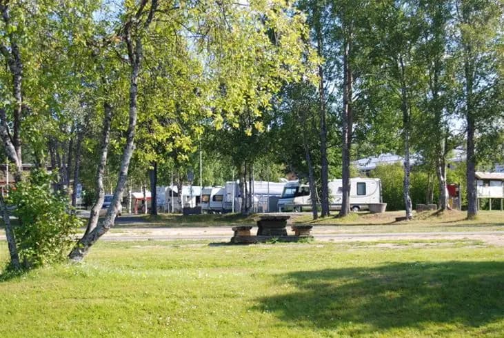 En grönskande campingplats omgiven av träd och gräs, med öppna ytor och inslag av skugga. En inbjudande miljö för besökare, typisk för Storuman.