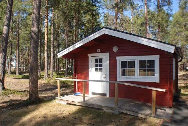En mysig timmerstuga med trädörr omgiven av grönskande natur på Storuman camping.