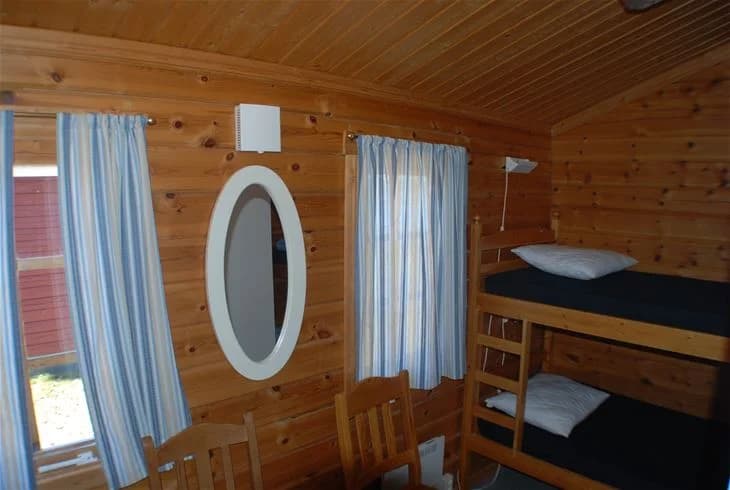 Ett interiört foto av en stuga på Storuman Camping, med trämöbler och trägolv. Rummet har en mysig atmosfär med ljusa trätak och bekvämligheter som en säng.