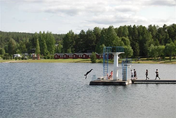 En campingplats vid en sjö, omgiven av grönska och berg, perfekt för rekreation och semester.