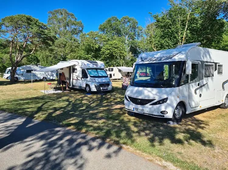 En parkerad husvagn på en campingplats vid Kneippbyn Resort Visby, omgiven av gröna träd och en klarblå himmel.