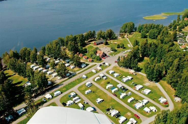 Fågelperspektiv över Frykenbadens camping vid kusten, med sjö och grönskande parklandskap.