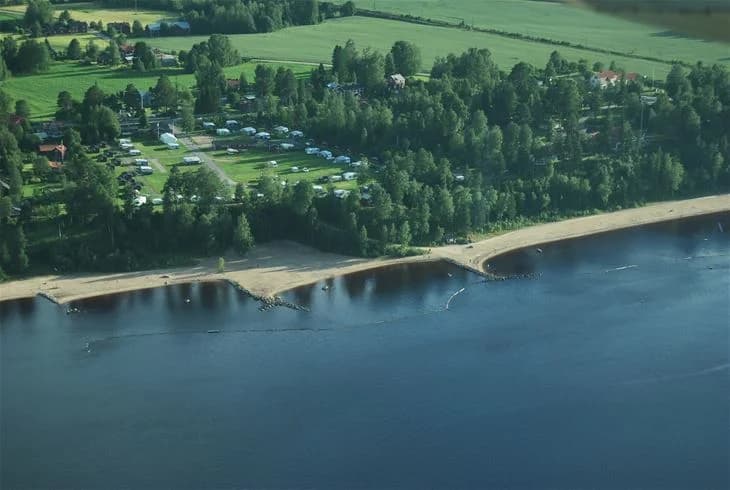 En vy över strandlinjen vid Orbadens camping, med en sjö och omgivande natur i bakgrunden.
