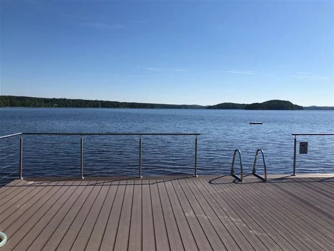 En liten träbrygga vid havet med trägolv, omgiven av vatten och trälandskap vid horisonten.