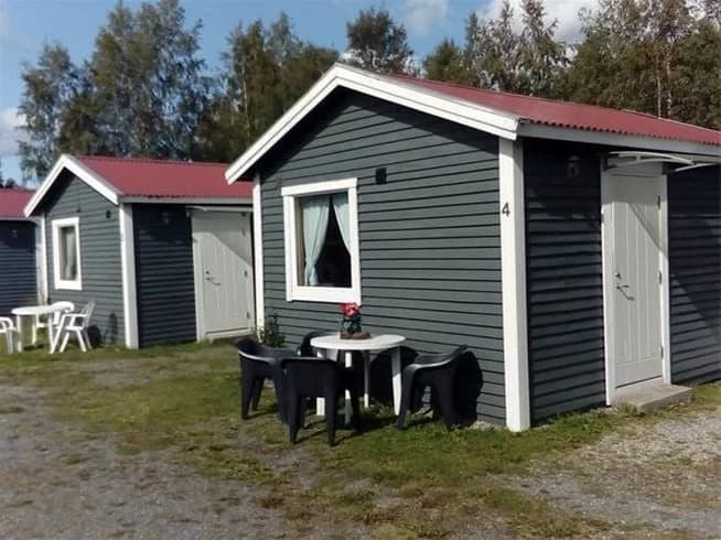 En mysig stuga omgiven av grönska på Antjärns camping, med utemöbler i en trädgårdsidyll.