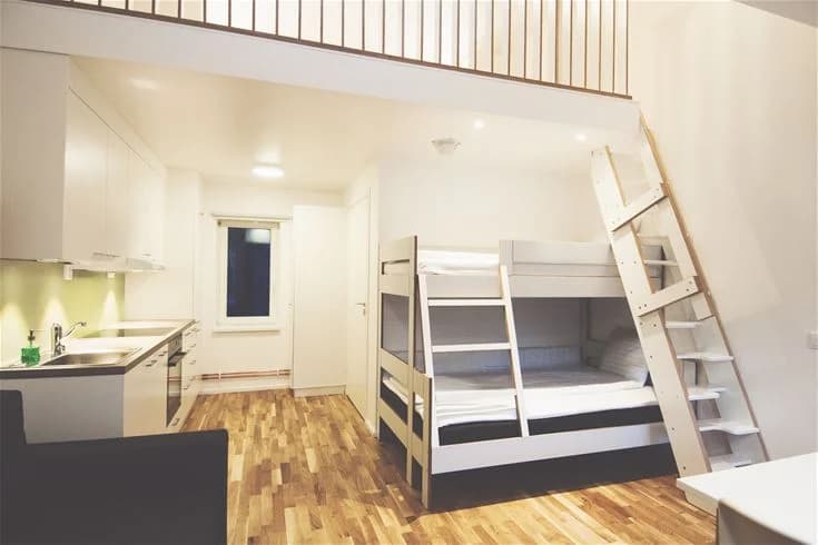 Ett enkelt, träbeklätt rum med ett trägolv och en takpanel. Rummet är inrett med två enkla sängar och ett fönster som släpper in naturligt ljus.