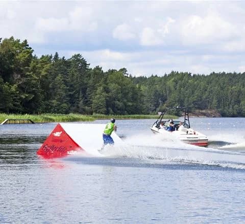 En motorbåt ligger förtöjd vid bryggan på Waxholms camping, med glittrande vatten och skog i bakgrunden, vilket skapar en inbjudande miljö för båt- och friluftsentusiaster.