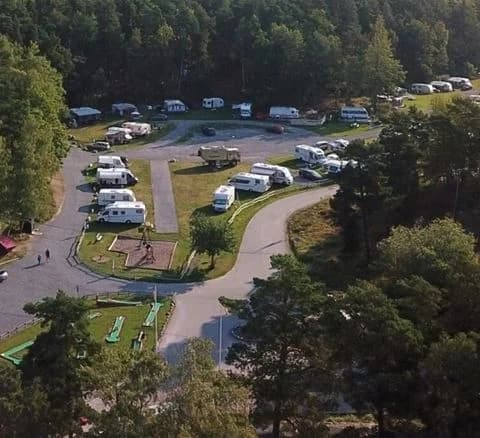 Flygbild över Waxholms camping som visar ett parkeringsområde med flera bilar, omgiven av grönska och välskötta landskapsytor.