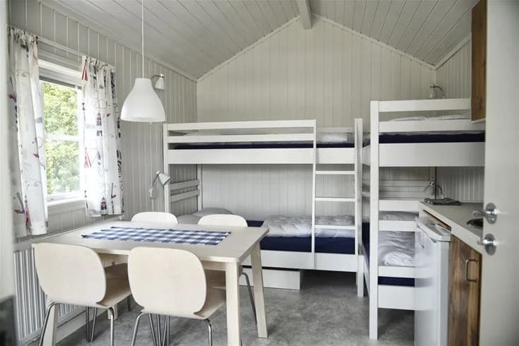 En mysig trästuga med ett sovrum som har en våningssäng och trägolv. Trädörrar syns i rummet, och taket har synliga träbjälkar. Avslappnad och inbjudande atmosfär.