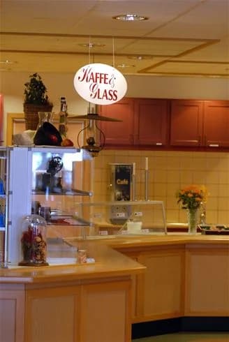 Bild av en stilren interiör på Gullbrannagården, med moderna ljusarmaturer som hänger från taket. Inredningen domineras av glas och trä, med en disk och en display med föremål. Atmosfären påminner om en restaurang med elegant och varm belysning.